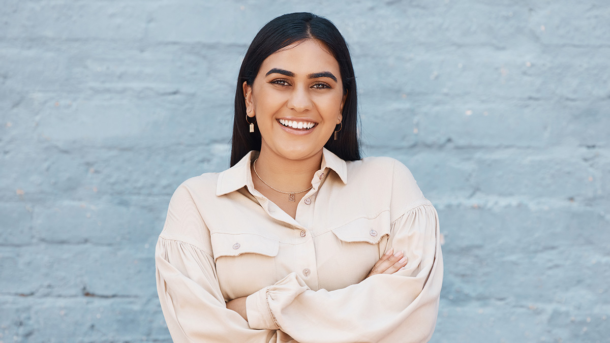 Professional woman against a blue brick wall and smiling towards the camera