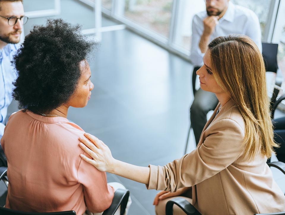 Two women engaged in a comforting conversation, emphasising support and empathy in the workplace